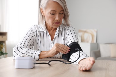 Woman measuring blood pressure at wooden table indoors