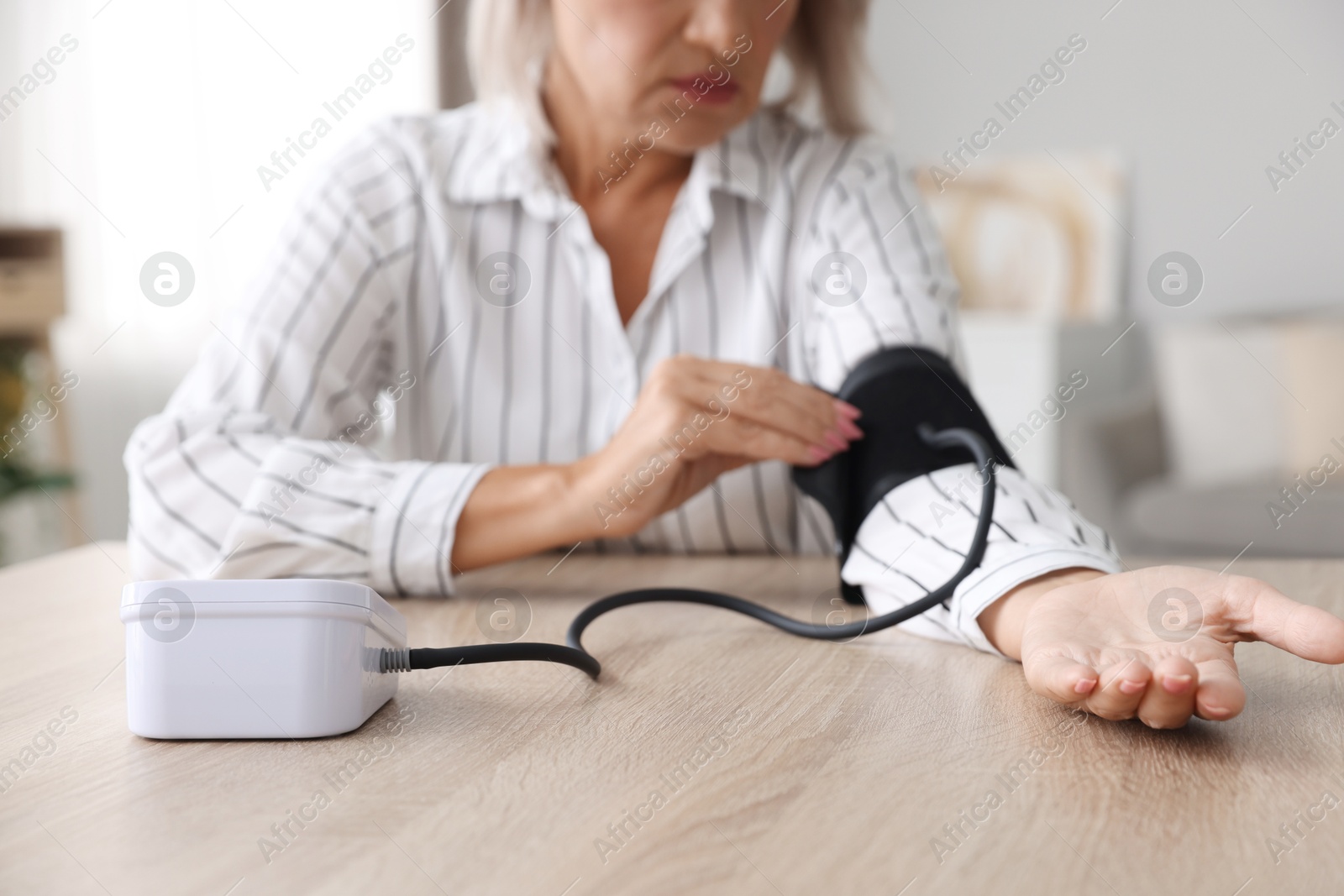 Photo of Woman measuring blood pressure at wooden table indoors, closeup