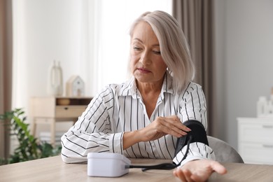 Photo of Woman measuring blood pressure at wooden table indoors