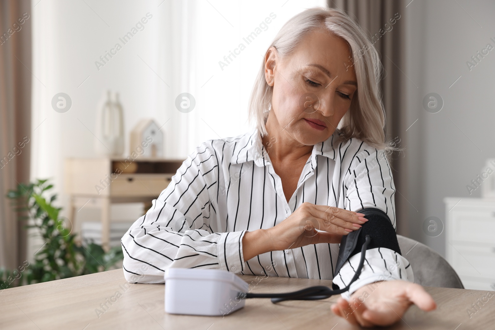 Photo of Woman measuring blood pressure at wooden table indoors