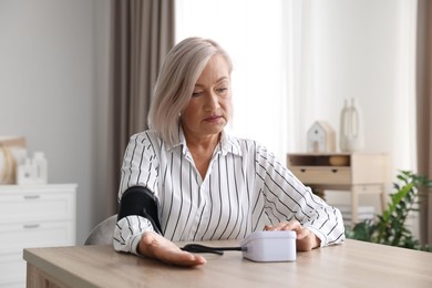 Photo of Woman measuring blood pressure at wooden table indoors