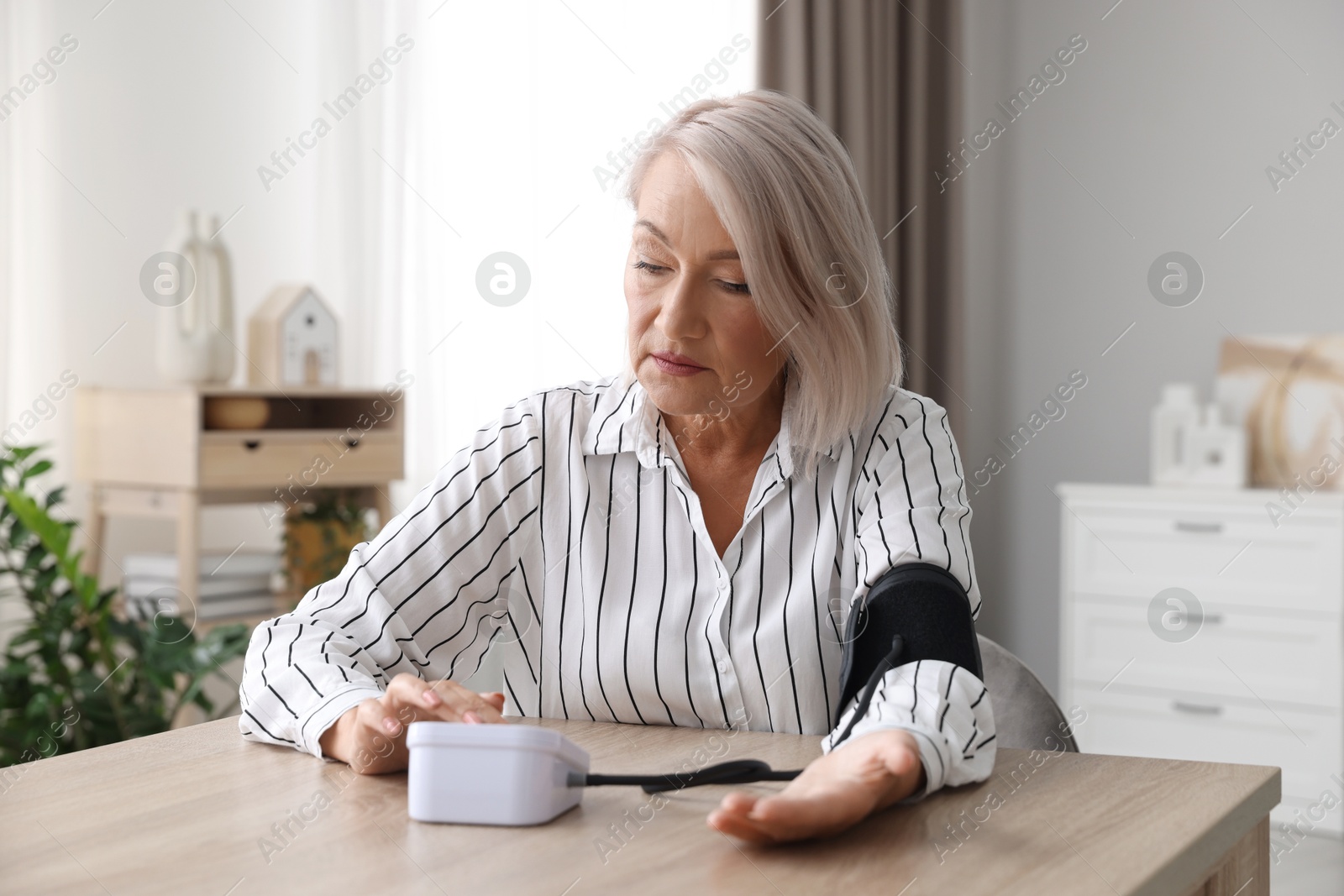 Photo of Woman measuring blood pressure at wooden table indoors