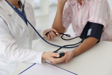 Photo of Doctor measuring patient's blood pressure at table in hospital, closeup