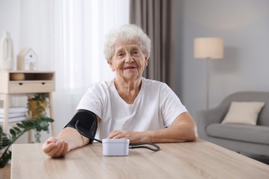 Photo of Senior woman measuring blood pressure at wooden table indoors