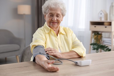 Photo of Senior woman measuring blood pressure at wooden table indoors