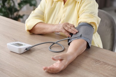 Photo of Senior woman measuring blood pressure at wooden table indoors, closeup