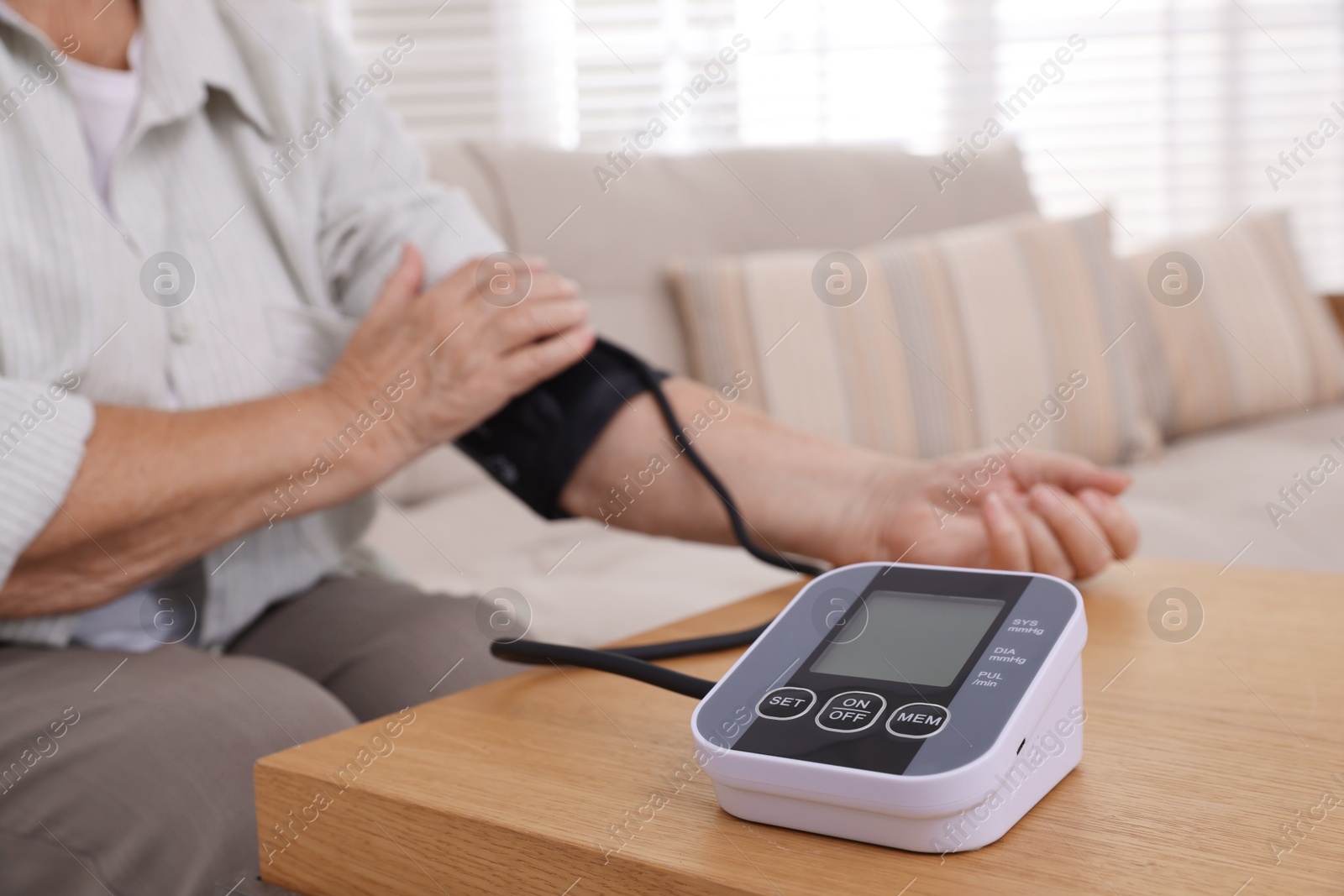 Photo of Senior woman measuring blood pressure at wooden table indoors, closeup