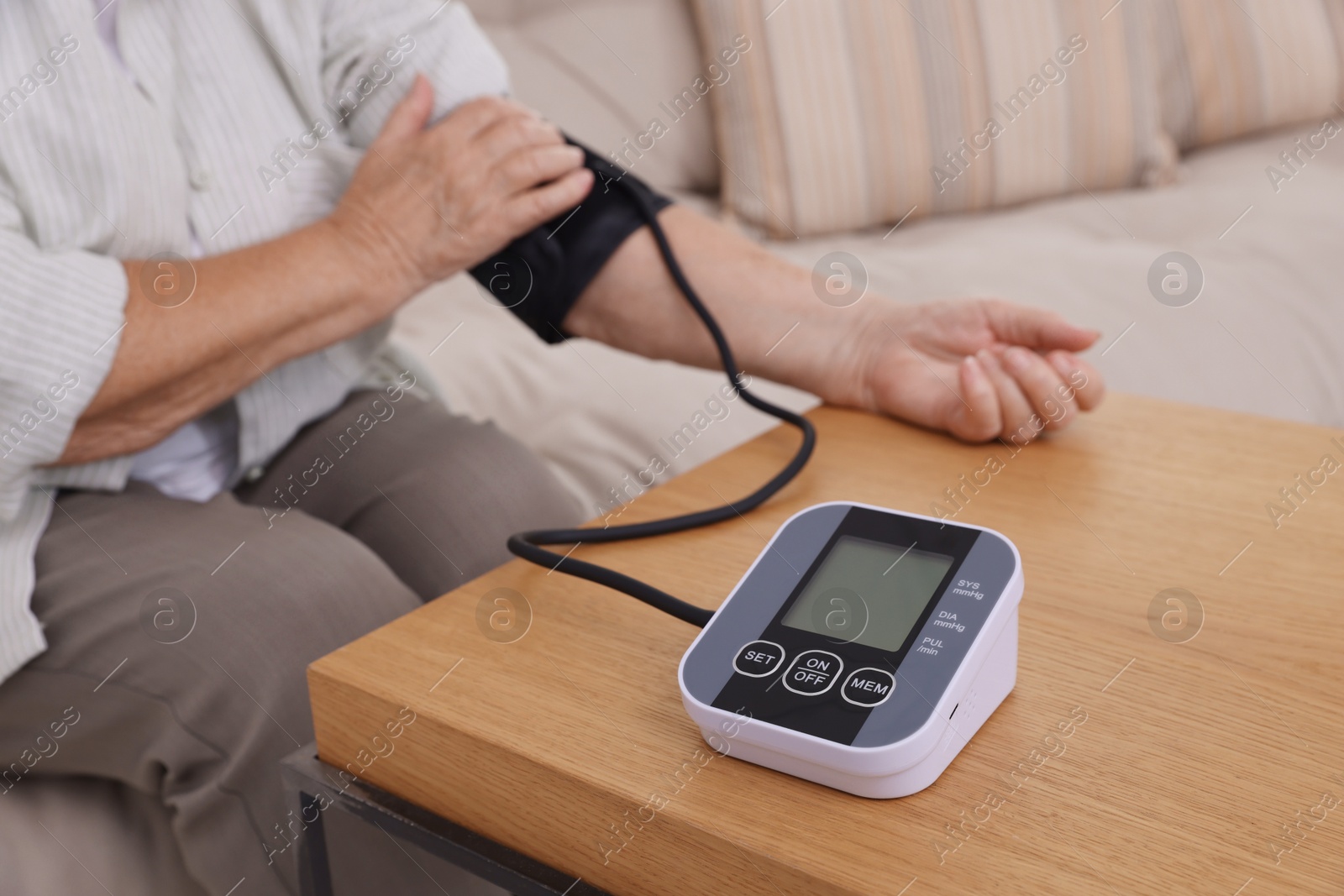 Photo of Senior woman measuring blood pressure at wooden table indoors, closeup