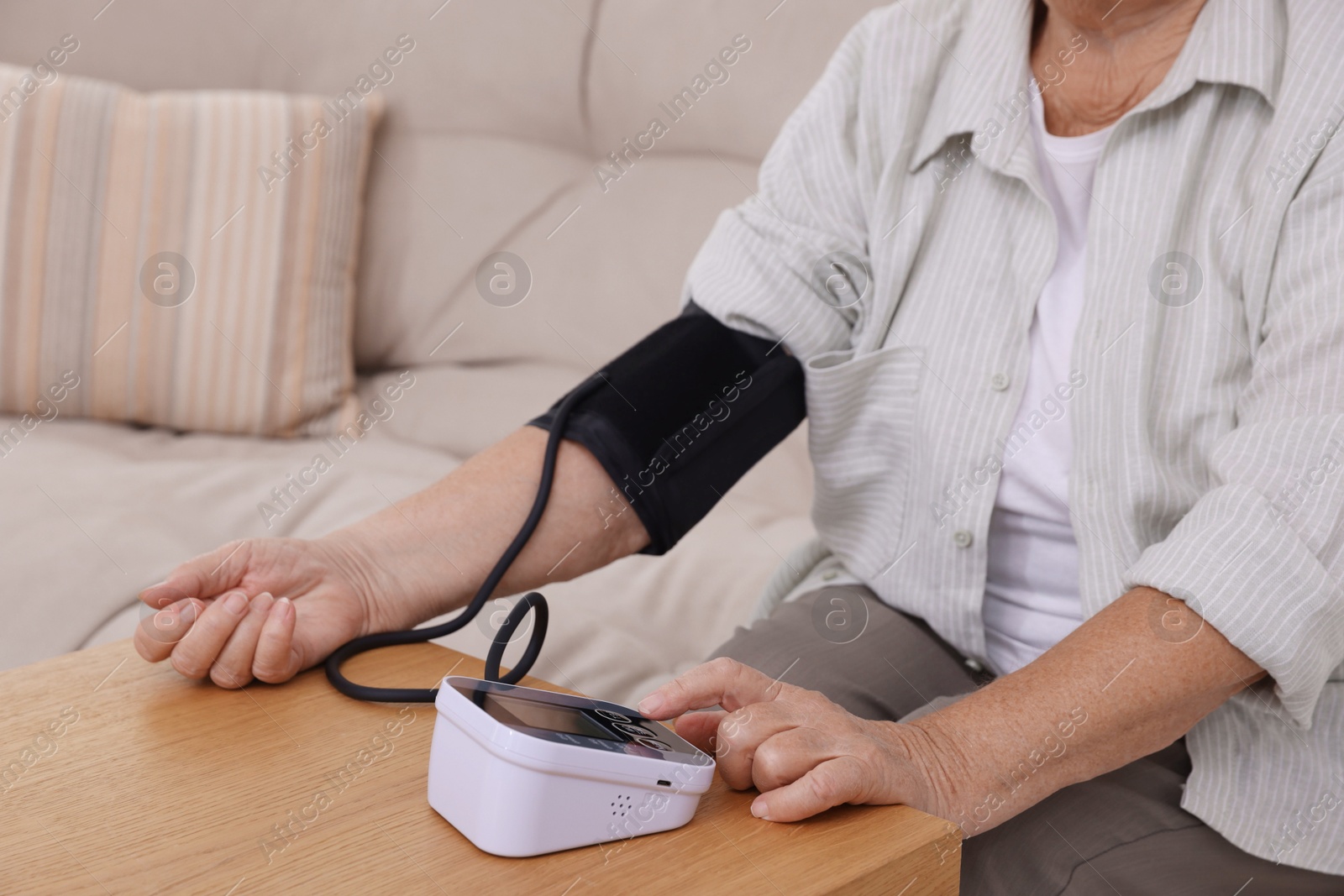 Photo of Senior woman measuring blood pressure at wooden table indoors, closeup