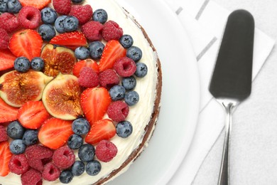 Photo of Delicious chocolate sponge cake with berries and server on light table, top view