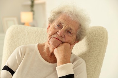 Photo of Pensive senior woman sitting on armchair at home