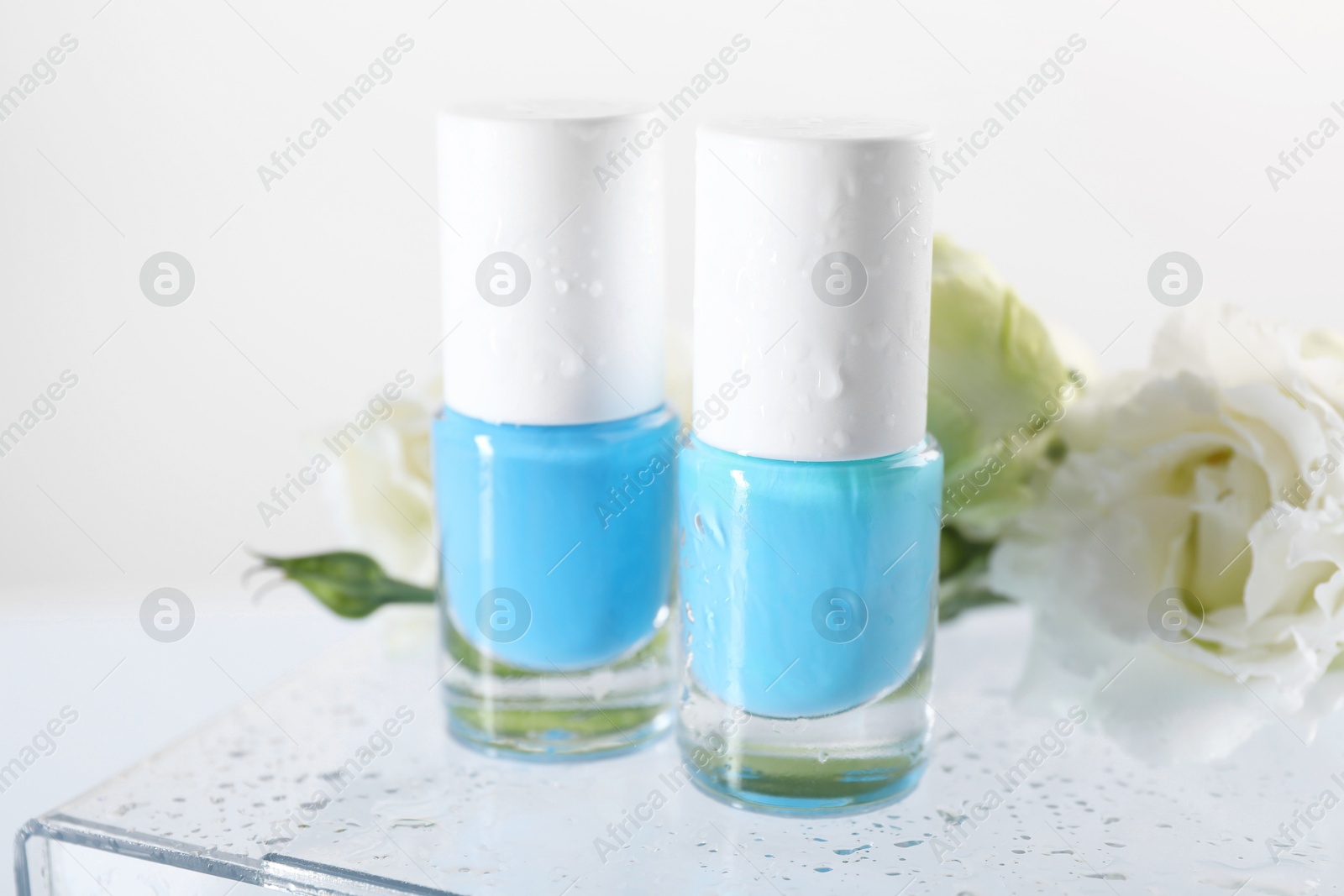 Photo of Nail polishes in bottles and beautiful flowers on light background, closeup