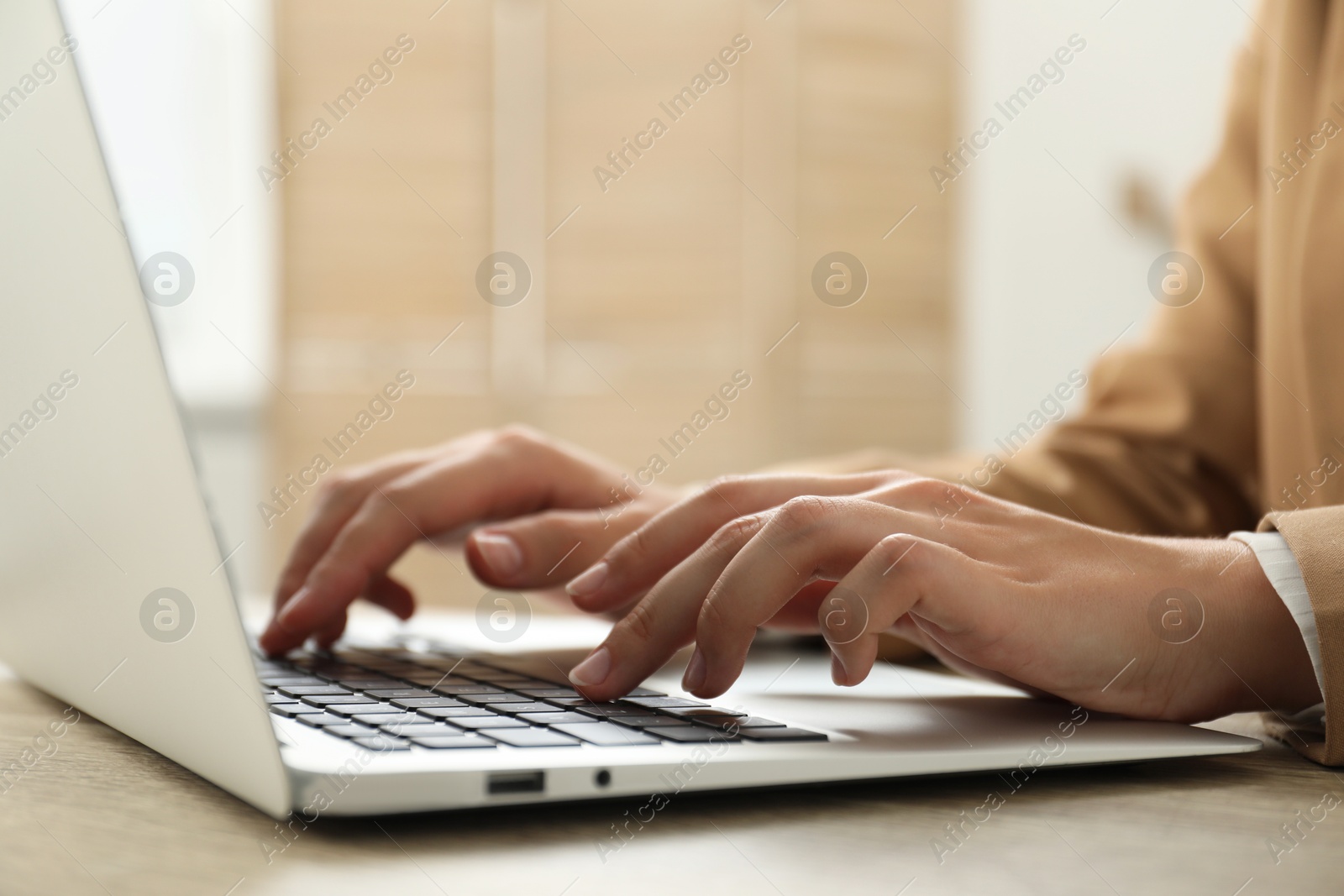 Photo of Businesswoman using laptop at wooden table indoors, closeup. Modern technology