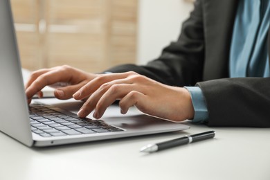 Photo of Businesswoman using laptop at white table indoors, closeup. Modern technology