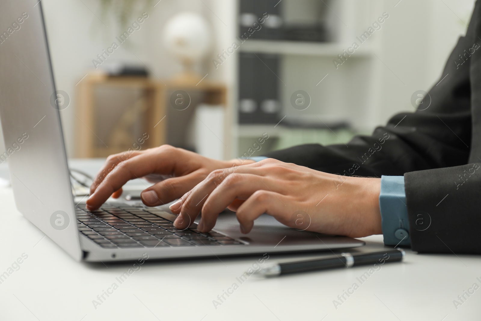 Photo of Businesswoman using laptop at white table indoors, closeup. Modern technology