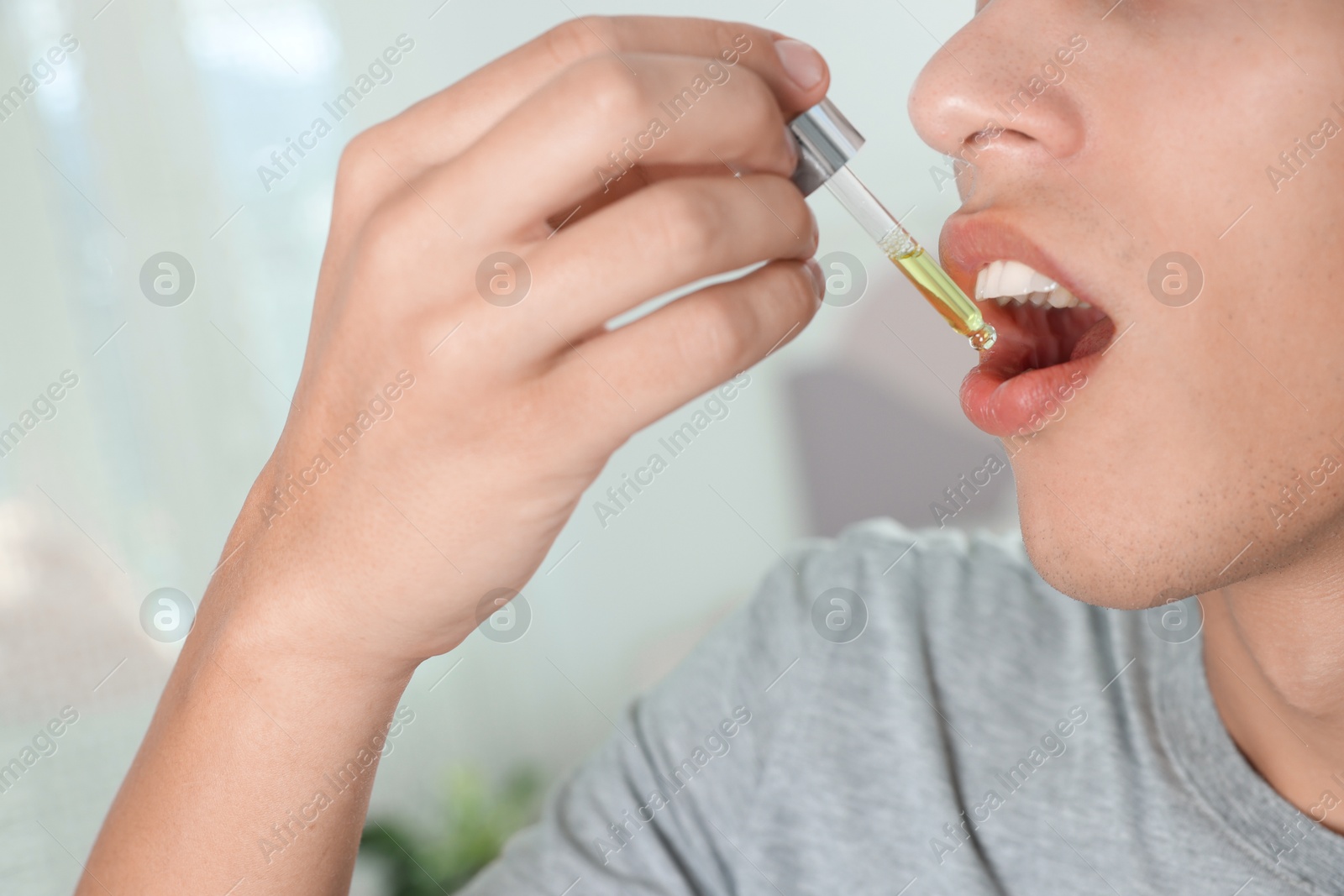 Photo of Young man taking CBD tincture indoors, closeup