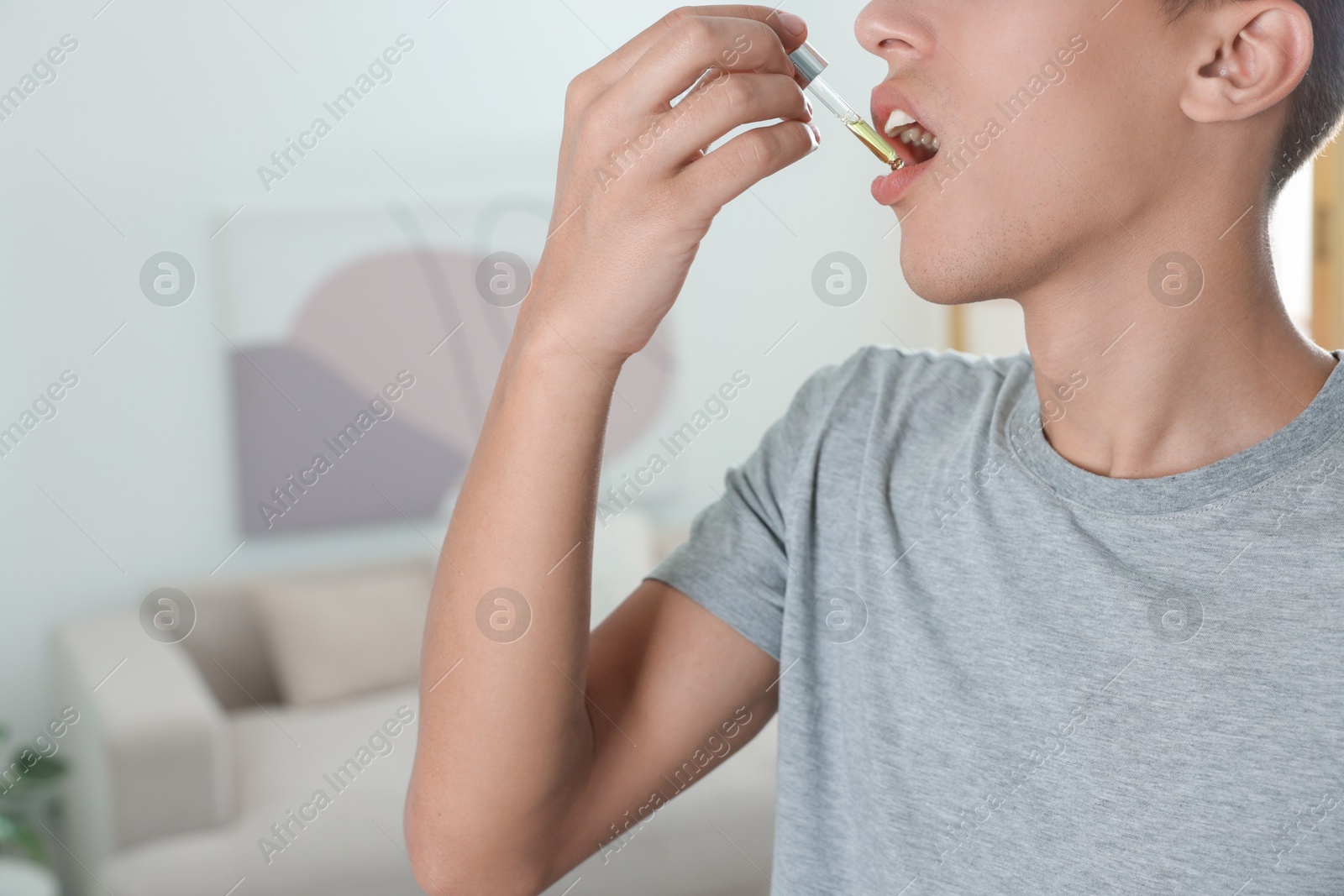 Photo of Young man taking CBD tincture indoors, closeup