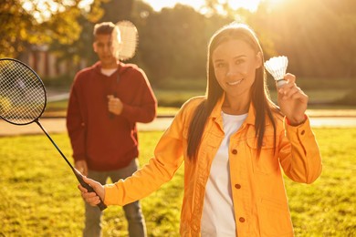 Photo of Young man and woman with badminton rackets and shuttlecock in park on sunny day, selective focus