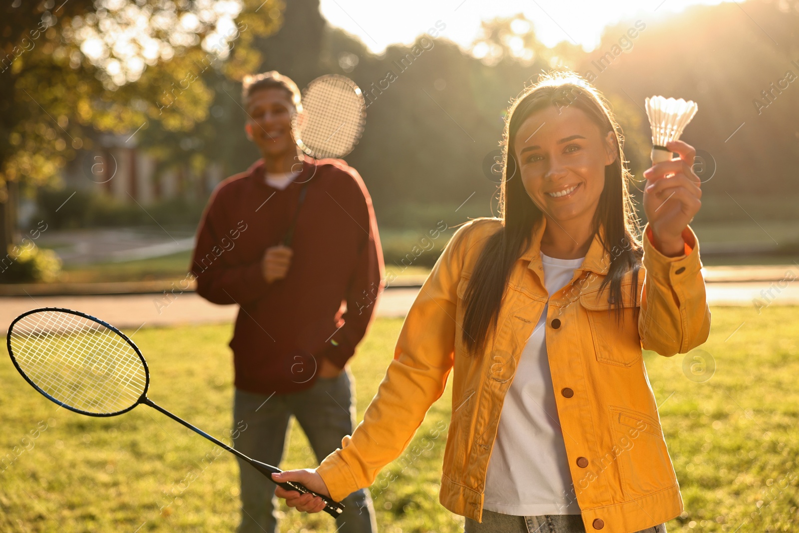 Photo of Young man and woman with badminton rackets and shuttlecock in park on sunny day, selective focus