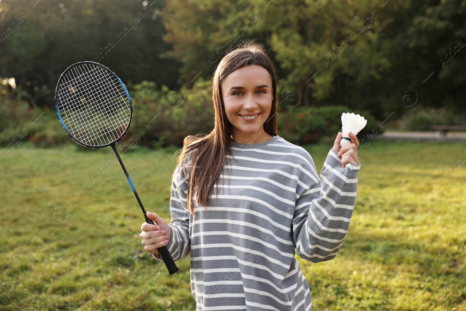 Photo of Happy young woman with badminton racket and shuttlecock in park