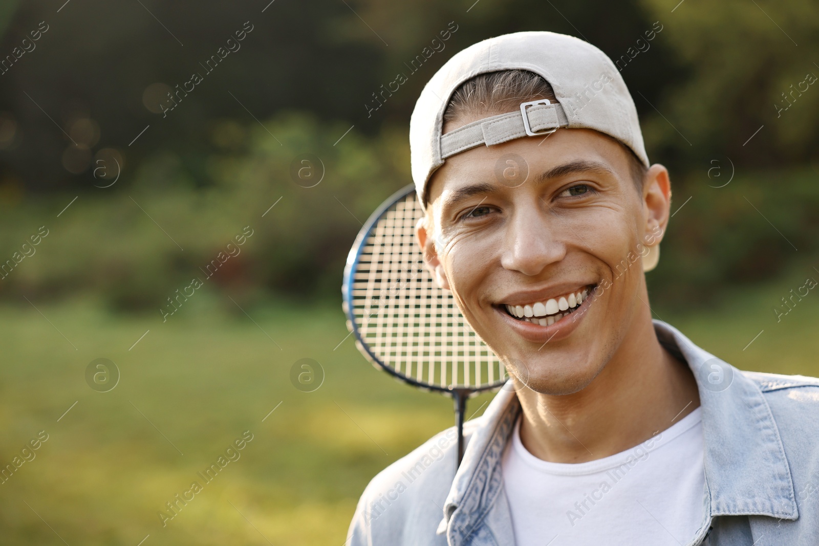 Photo of Happy young man with badminton racquet in park, space for text