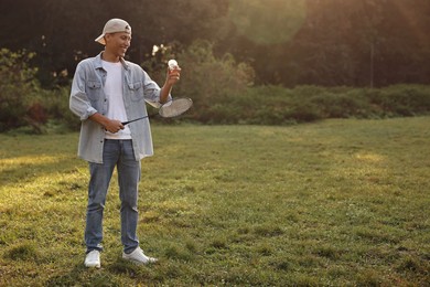 Photo of Happy young man with badminton racket and shuttlecock in park, space for text