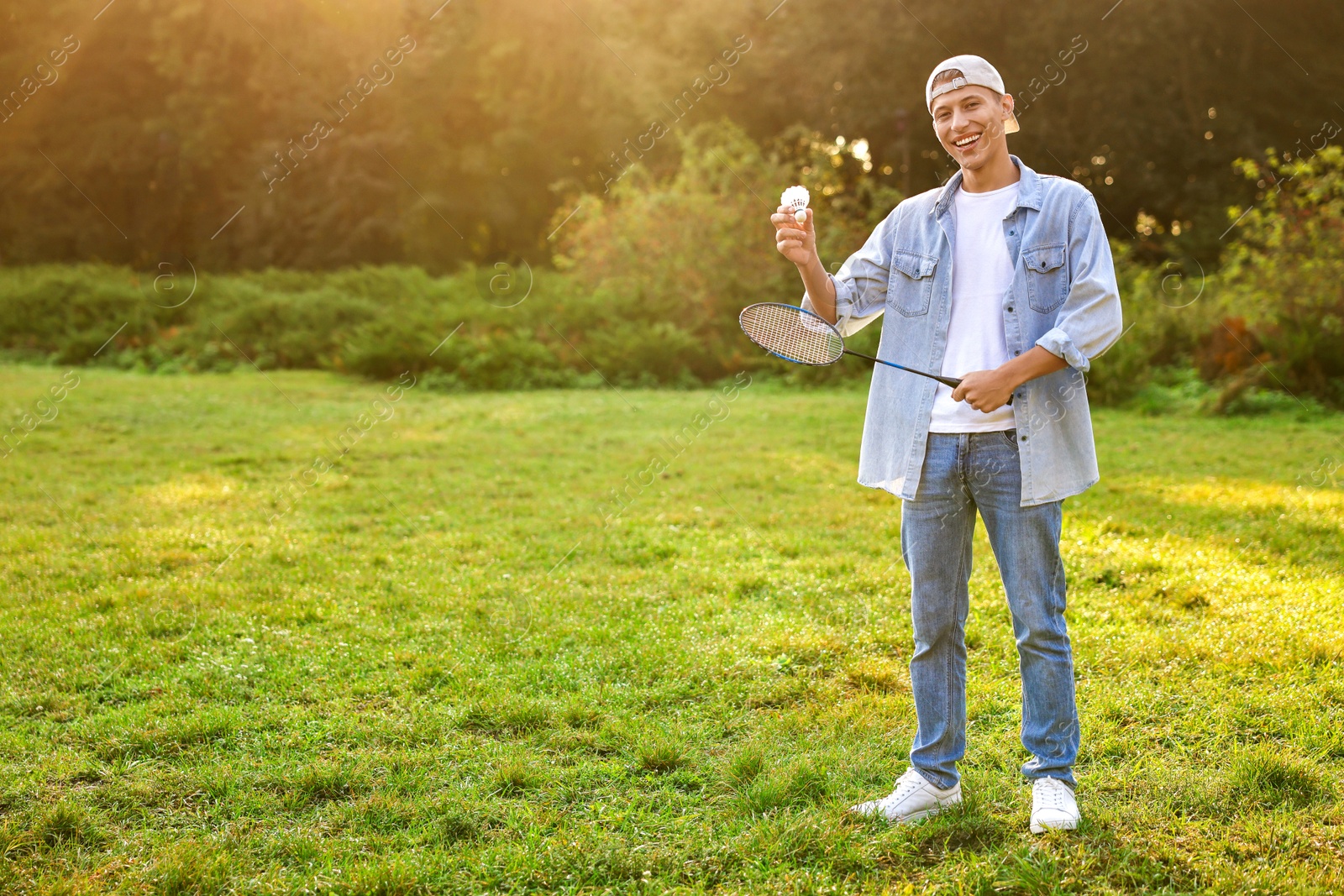 Photo of Happy young man with badminton racket and shuttlecock in park, space for text