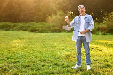 Happy young man with badminton racket and shuttlecock in park, space for text