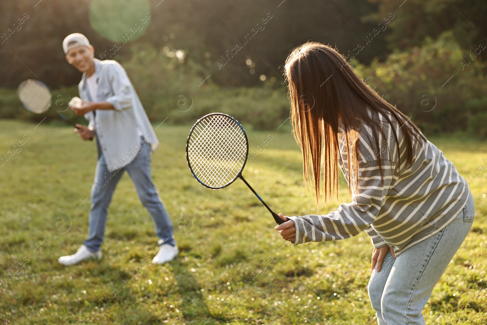 Photo of Young man and woman playing badminton in park on sunny day, selective focus