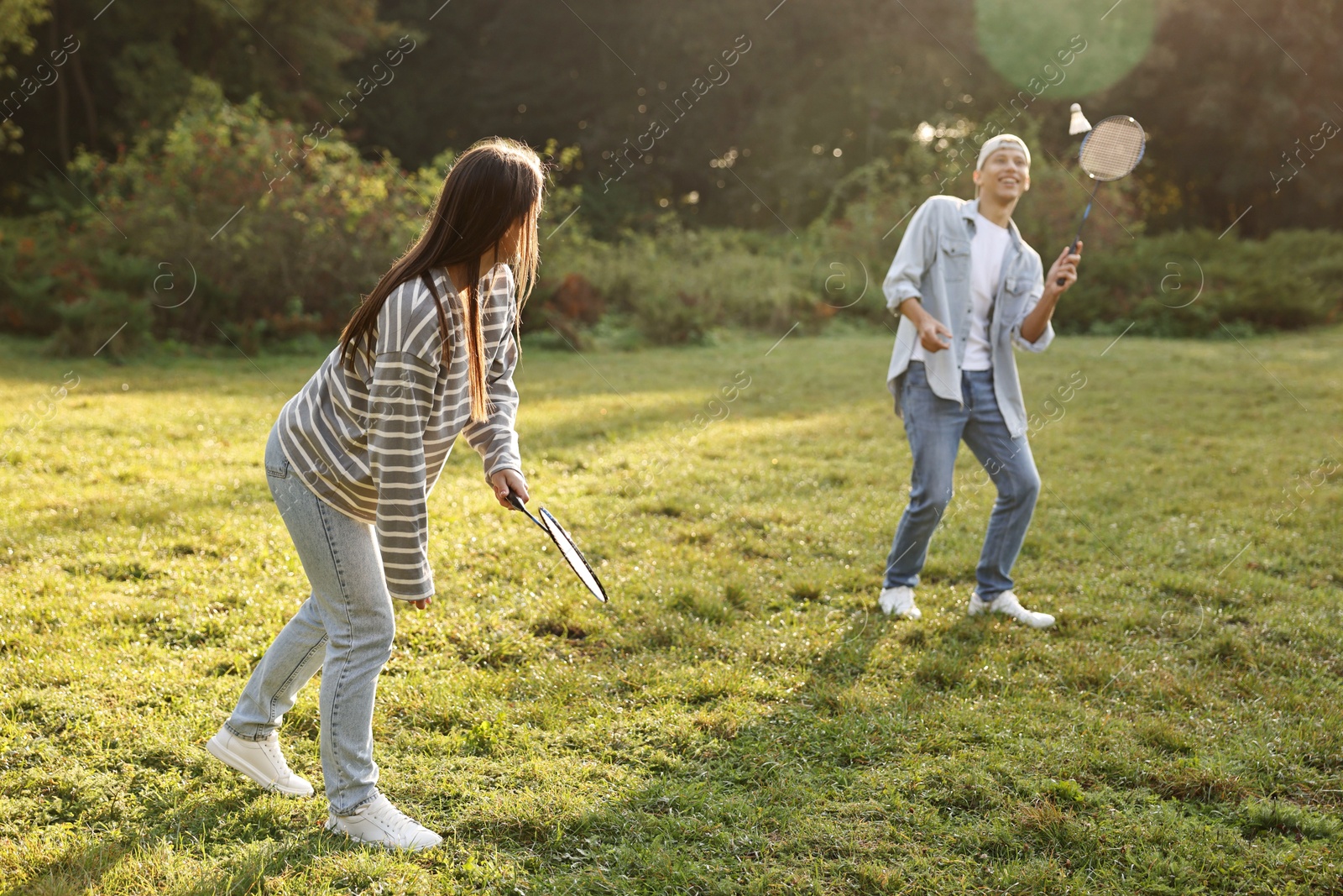 Photo of Young man and woman playing badminton in park on sunny day, selective focus