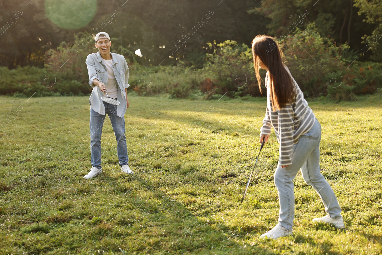 Photo of Young man and woman playing badminton in park on sunny day, selective focus