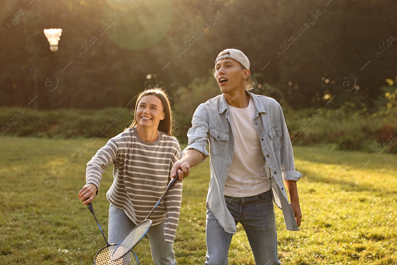 Photo of Young woman and man playing badminton in park on sunny day