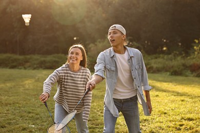 Photo of Young woman and man playing badminton in park on sunny day