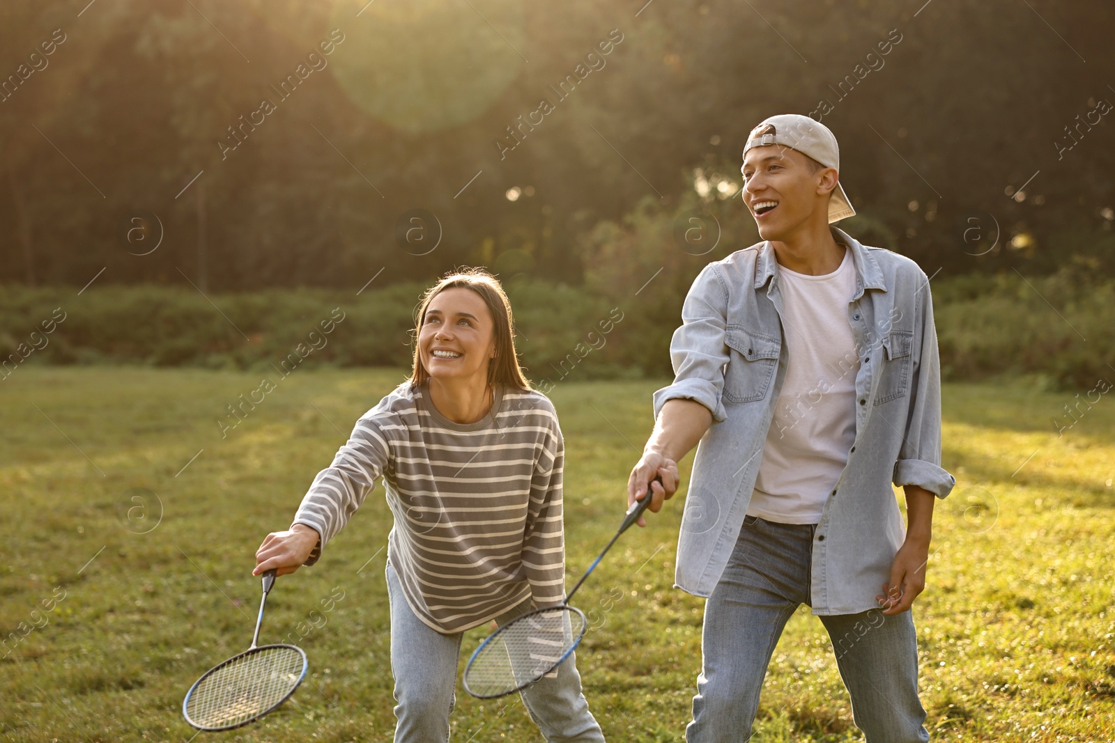 Photo of Young woman and man playing badminton in park on sunny day