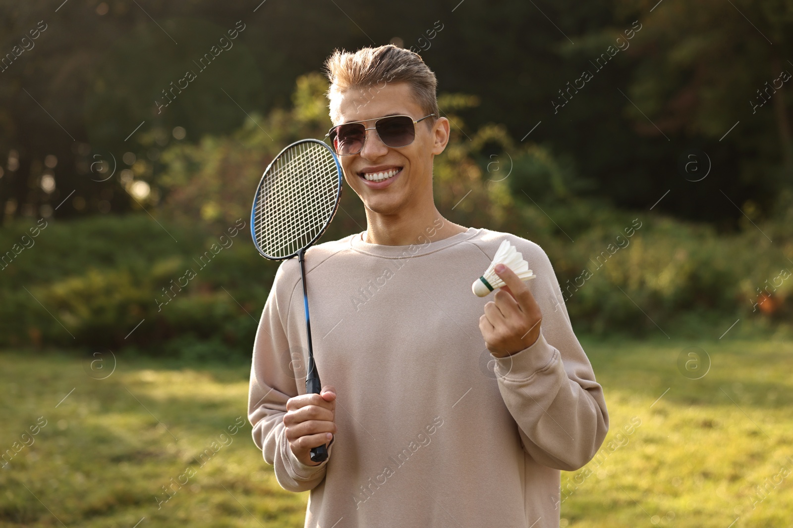 Photo of Happy young man with badminton racket and shuttlecock in park on sunny day