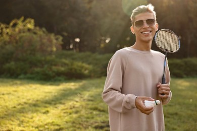 Photo of Happy young man with badminton racket and shuttlecock in park on sunny day, space for text