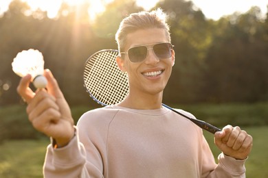 Photo of Happy young man with badminton racket and shuttlecock in park on sunny day