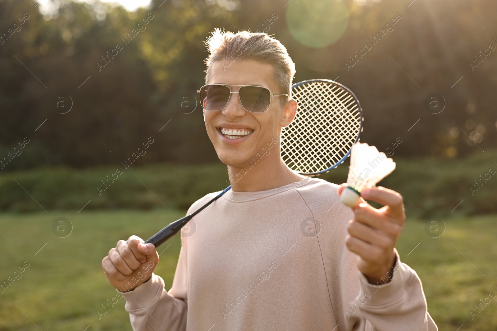 Photo of Happy young man with badminton racket and shuttlecock in park on sunny day