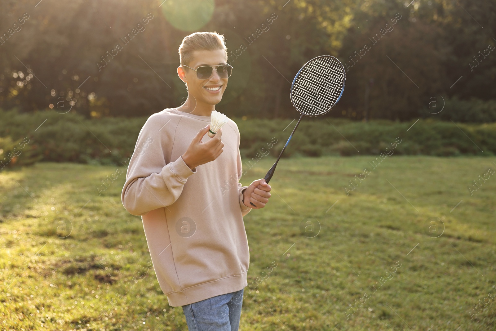 Photo of Happy young man with badminton racket and shuttlecock in park on sunny day