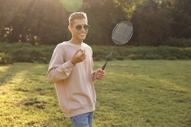 Happy young man with badminton racket and shuttlecock in park on sunny day