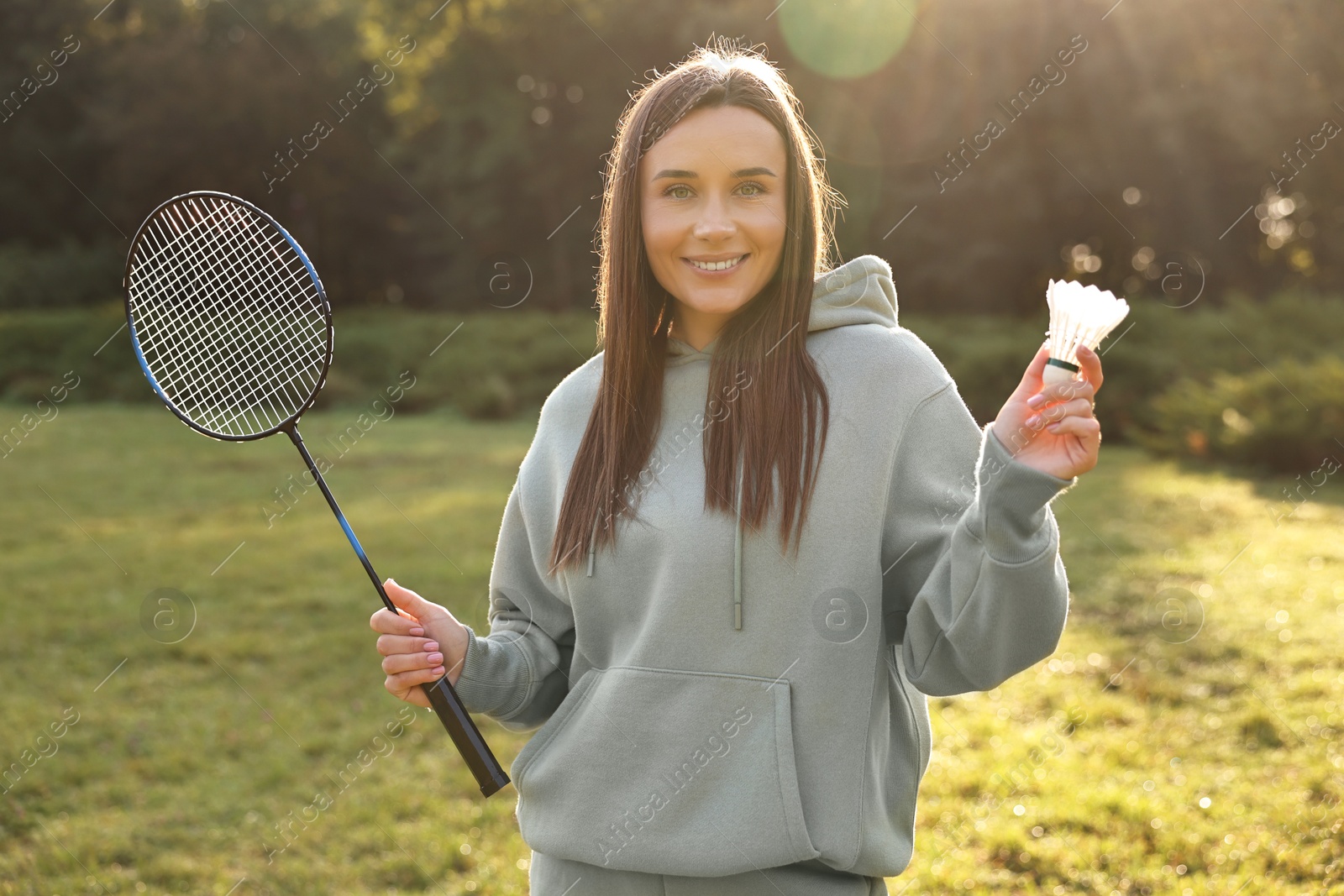 Photo of Happy young woman with badminton racket and shuttlecock in park on sunny day