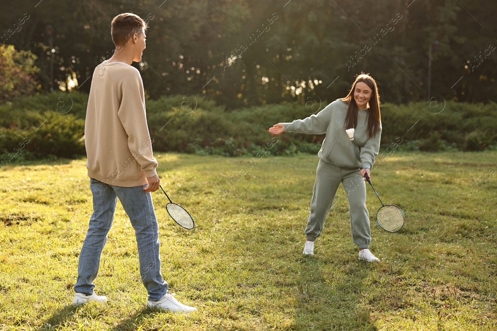 Photo of Young woman and man playing badminton in park on sunny day, selective focus