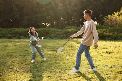 Photo of Young woman and man playing badminton in park on sunny day, selective focus