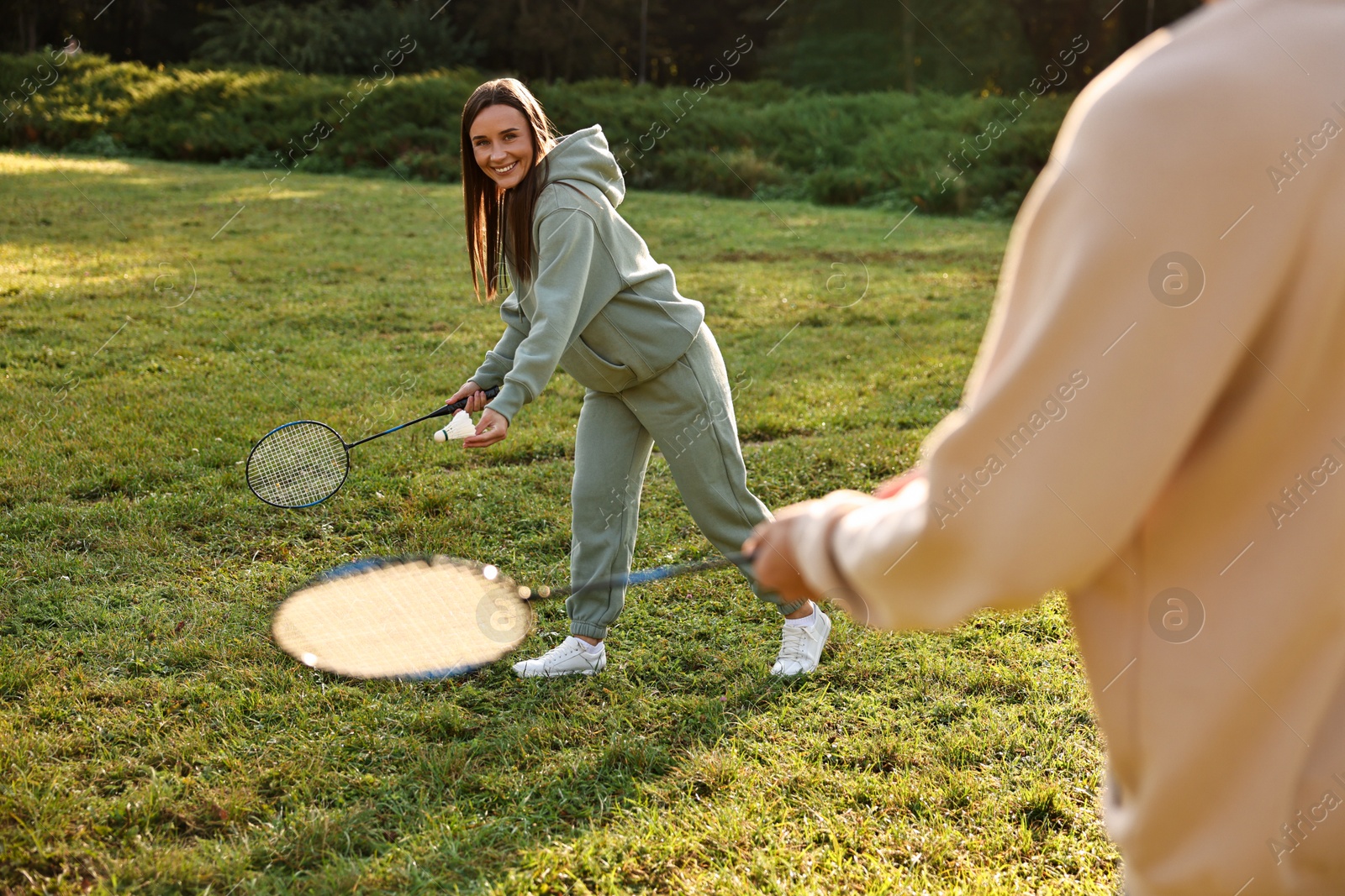 Photo of Young woman and man playing badminton in park on sunny day, selective focus