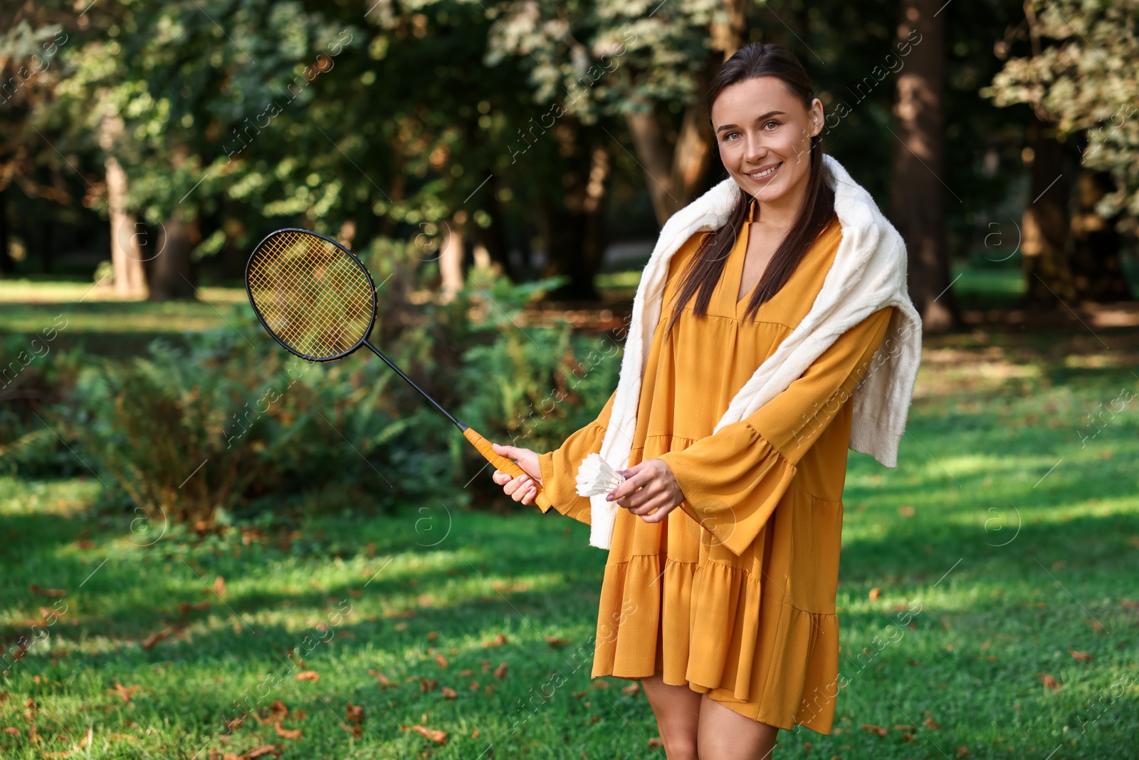 Photo of Happy young woman with badminton racket and shuttlecock in park