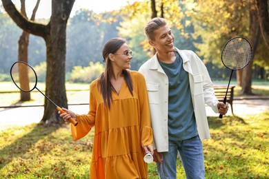 Photo of Young man and woman with badminton rackets and shuttlecock in park on sunny day