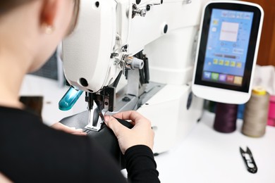 Photo of Woman working with sewing machine at white table in professional workshop, closeup