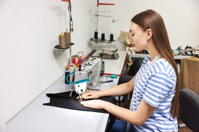 Photo of Young woman working with sewing machine in professional workshop