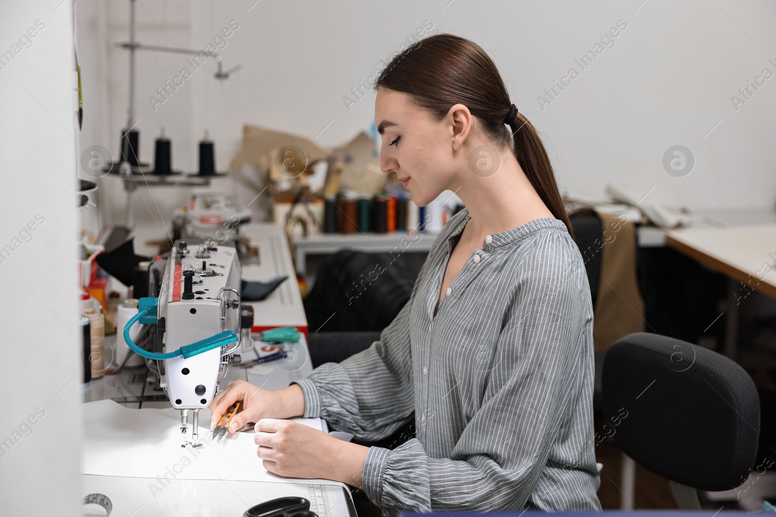 Photo of Young woman working with sewing machine in professional workshop