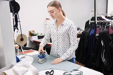 Photo of Young woman with iron working at white table in professional workshop